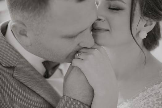 A man and woman are kissing each other's hands. The man is wearing a wedding ring photo