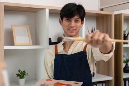 Young Artist Holding Paintbrush in Studio with Shelves and Plants in Background photo