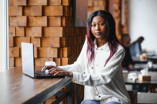 Young African American girl sitting in restaurant and typing on her laptop. Pretty girl working on computer at cafe. photo