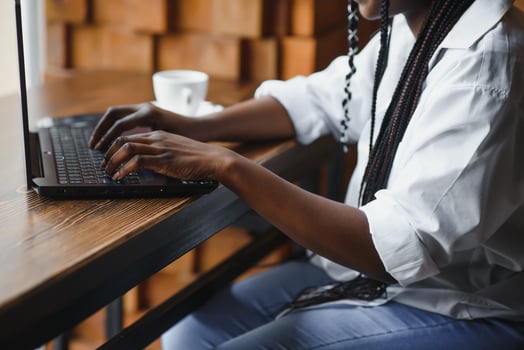 Young African American girl sitting in restaurant and typing on her laptop. Pretty girl working on computer at cafe. photo