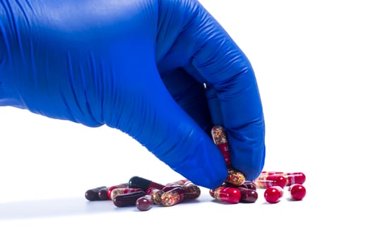 Hand in blue glove holding pill isolated on white background. photo