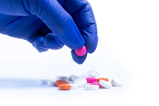 Hand of doctor or nurse wearing blue gloves takes pink pills from multicolored pills on white background. photo