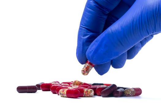 Hand in blue gloves holding red pill isolated on a white background. Closeup photo