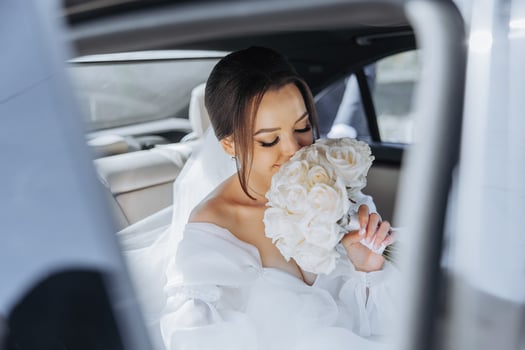 A bride is getting into a car with a bouquet of white roses. The scene is intimate and romantic, with the bride looking into the car and the roses symbolizing love and commitment photo