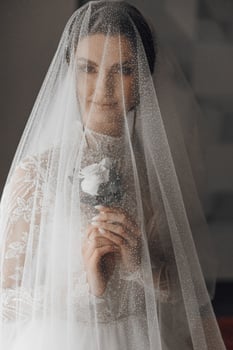 A woman is wearing a veil and holding a flower. The veil is white and covers her face photo