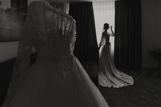 A bride is standing in front of a dresser with a white dress on. The dress is hanging on a hanger and is the bride's wedding dress photo