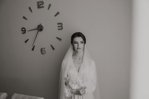 A woman in a wedding dress stands in front of a clock with the hands on the numbers 9 and 3 photo