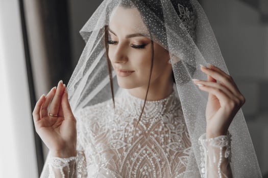 A woman in a wedding dress is wearing a veil and holding her hands up. Concept of elegance and celebration, as the bride is getting ready for her wedding day photo