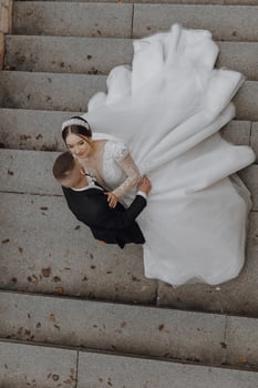 A bride and groom are standing on a staircase, with the bride wearing a long white dress. The man is wearing a suit and the woman is wearing a tiara. Scene is romantic and happy photo