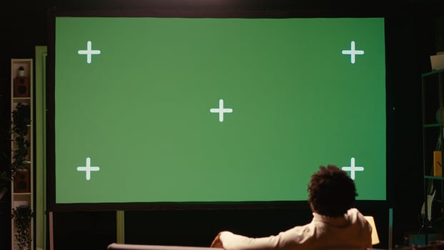 Man using green screen modern TV to watch news program broadcasting in living room. Person watching mockup ultrawide television display showing VOD channel, relaxing on couch photo