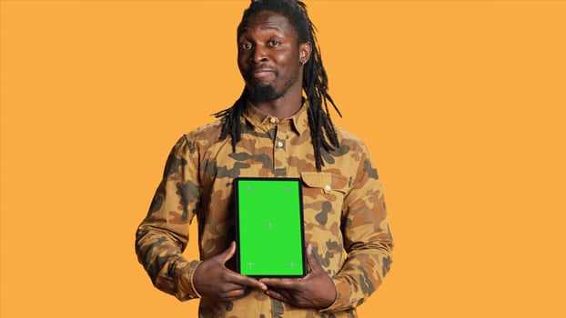 African american adult with greenscreen on gadget, presenting isolated chromakey display and smiling in front of camera. Young adult holding mobile device with copyspace blank layout. photo
