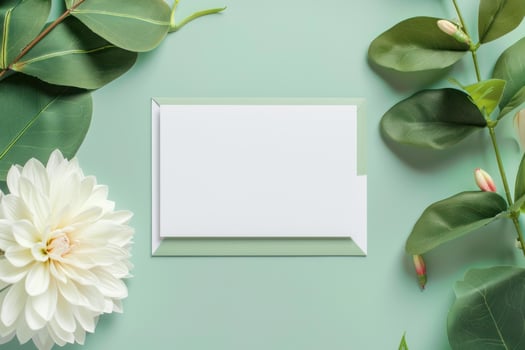 Blank greeting card surrounded by white dahlia flower and green leaves on pastel green background photo