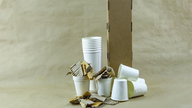 White paper coffee cup, used paper, and cardboard box on a brown surface, awaiting recycling. photo