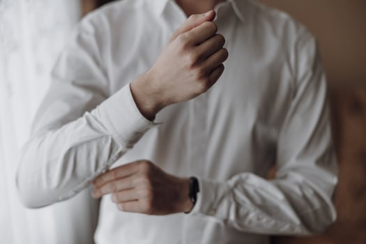 A man is getting dressed in a white shirt and is adjusting his shirt sleeves. Concept of formality and attention to detail, as the man is taking the time to properly dress himself photo