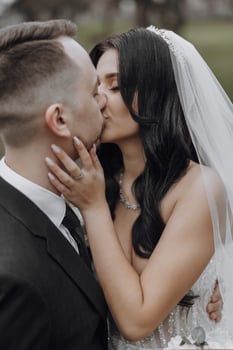 A bride and groom kiss in a wedding photo. The bride is wearing a veil and the groom is wearing a tie photo