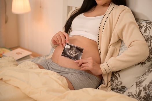 Pregnant woman holding ultrasound picture in bedroom photo