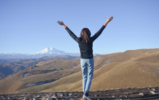 A young brunette woman with her hands raised up against the backdrop of the snow-capped Mount Elbrus. photo