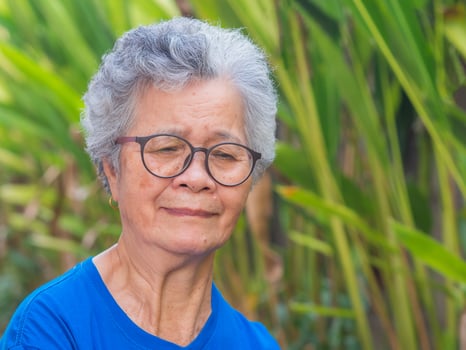 Portrait of a senior woman with short gray hair wearing glasses and looking down while standing in a garden. Space for text. Concept of aged people and healthcare photo
