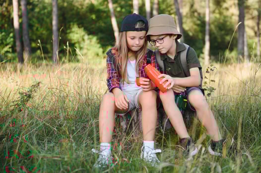 Girl and boy scout sitting and drinking hot tea from thermos in the woods photo