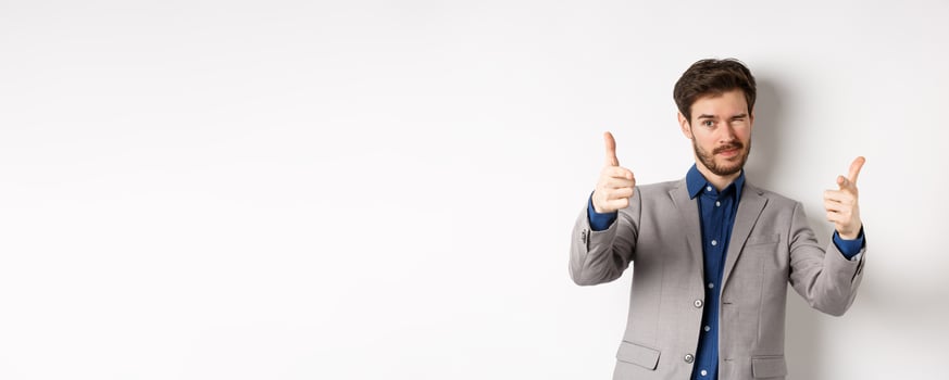 You got this. Handsome caucasian businessman in suit pointing fingers at camera and winking, motivating people, inviting to work in company, standing on white background photo