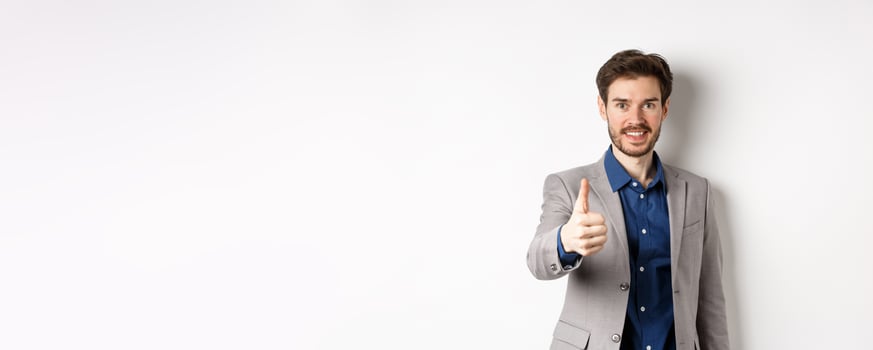 Image of handsome businessman in suit showing thumb up and smiling, standing on white background photo