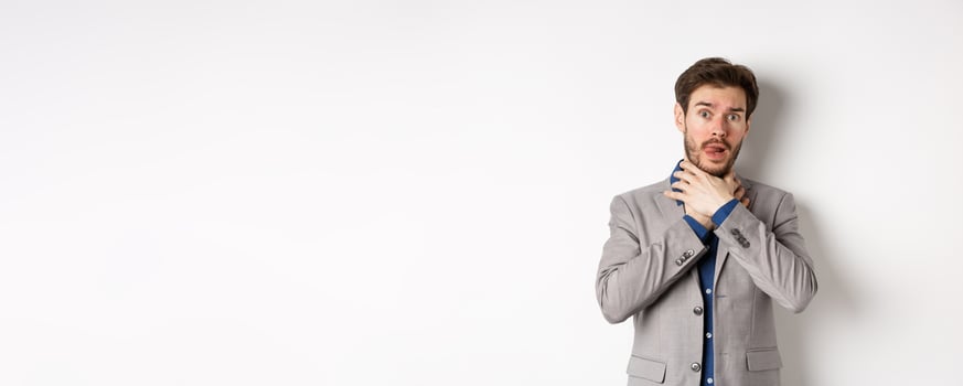 Distressed young man in business suit strangle himself and showing tongue, feeling sick with sore throat, standing on white background photo