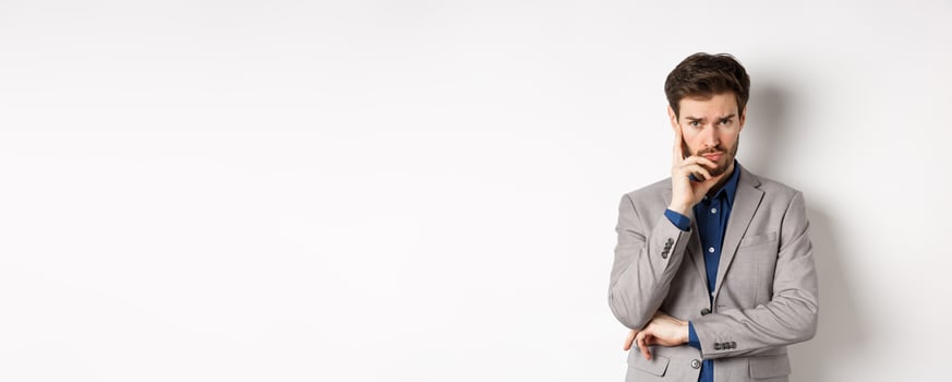 Troubled frowning business man in suit looking at camera pensive, thinking or making decision, standing on white background photo