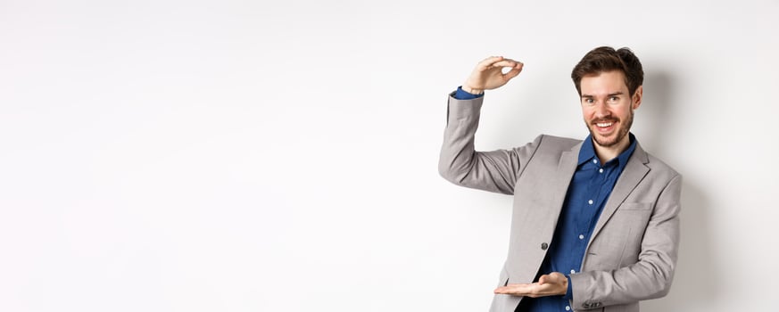 Successful businessman showing big size, shape large object and smiling pleased, standing on white background in suit photo