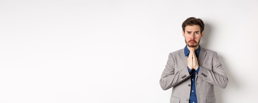 Miserable whining businessman asking for loan, need help and begging you, sobbing and say please with sad face, standing on white background, ask for forgiveness photo