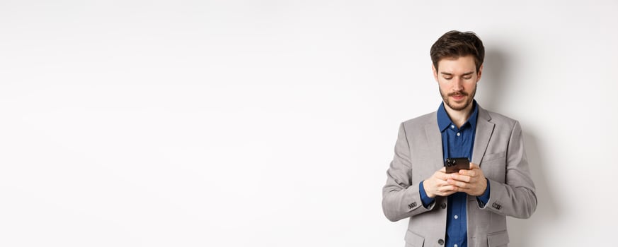 Businessman chatting on mobile phone, standing in suit with serious face, white background photo