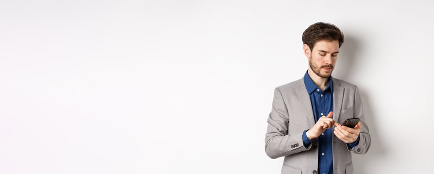 Handsome businessman in stylish suit chatting on smartphone, using mobile phone, standing on white background photo