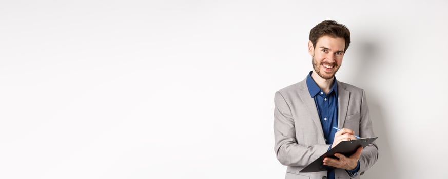 Smiling male manager in suit writing on clipboard, taking notes at office meeting, standing on white background photo