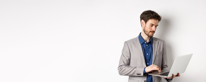 Handsome male entrepreneur working on laptop, looking serious at screen, standing against white background photo