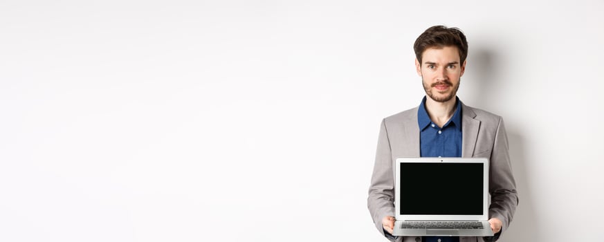 Handsome caucasian businessman in suit showing empty laptop screen, demonstrate promo, standing on white background photo