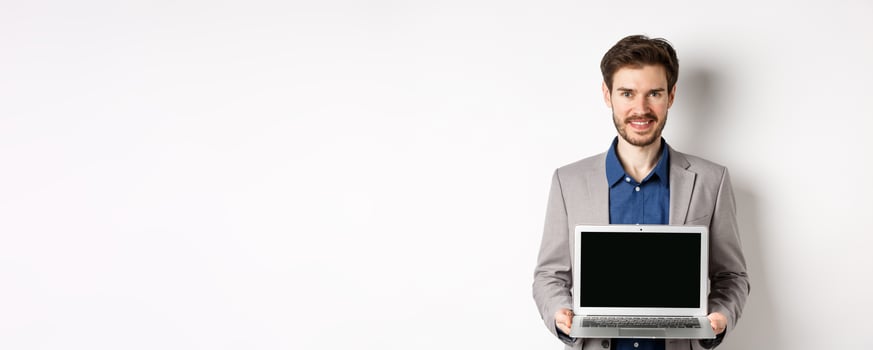 Handsome caucasian businessman in suit showing empty laptop screen, demonstrate promo, standing on white background photo
