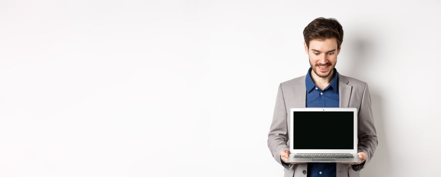 Handsome caucasian businessman in suit showing empty laptop screen, demonstrate promo, standing on white background photo