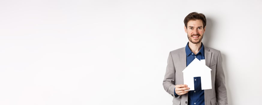 Real estate. Handsome young businessman buying property, holding paper house cutout and smiling, agency advertisement, white background photo