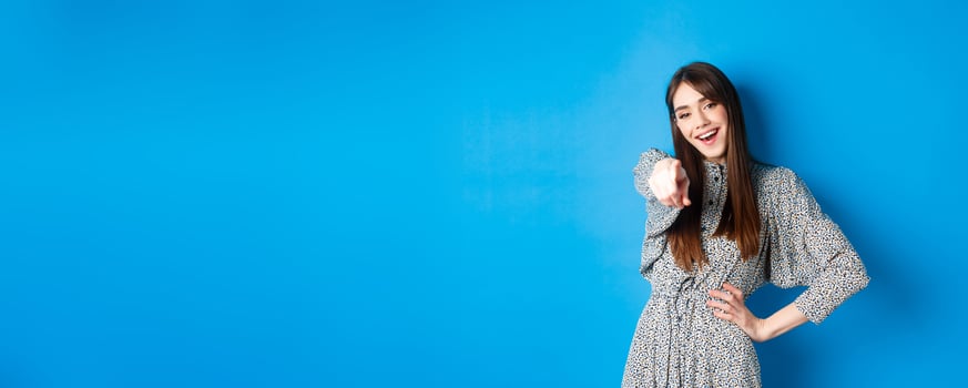 Motivated and excited young woman pointing finger at camera and smiling, congratulating you, praising or inviting, standing happy on blue background photo
