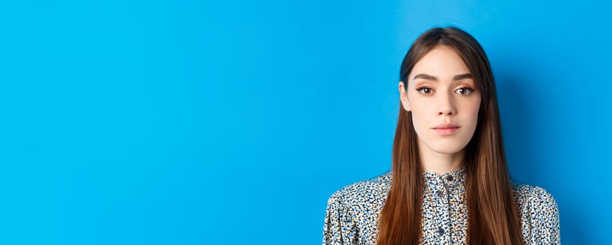 Close-up of candid beautiful woman with long natural hair and makeup, looking at camera, standing on blue background photo