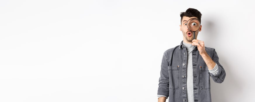 Image of excited guy look through magnifying glass, gasping amazed, big eye staring at interesting thing, found cool promo, standing on white background photo