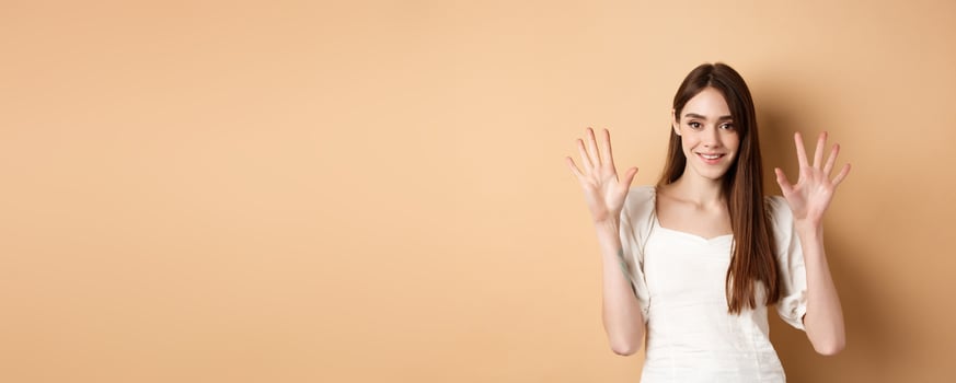 Attractive young woman show fingers number ten, smiling and looking confident, standing on beige background photo