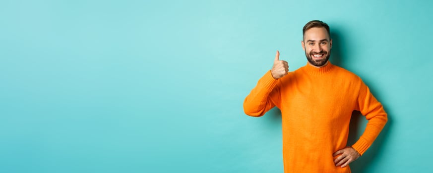 Well done. Handsome bearded man showing thumb up, praising good work, recommend excellent product, like and approve, smiling satisfied, standing over light blue background photo