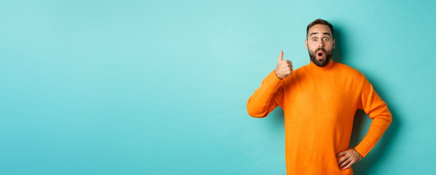 Well done. Handsome bearded man showing thumb up, praising good work, recommend excellent product, like and approve, smiling satisfied, standing over light blue background photo