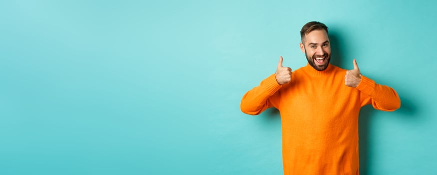Handsome man expressing support, showing thumb up, encourage you, praise excellent work, approve and agree, standing over light blue background photo
