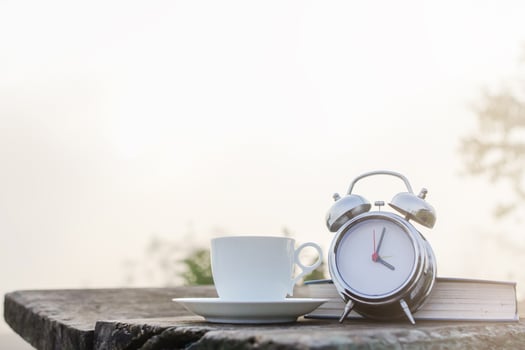 A white coffee cup and an alarm clock are placed beside the Bible on a wooden table in the morning to prepare for Bible study and watch the beautiful scenery in the morning after drinking coffee. photo