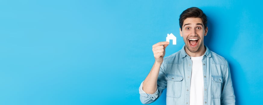 Real estate concept. Happy young man looking excited, found apartment, showing small house model, standing over blue background photo