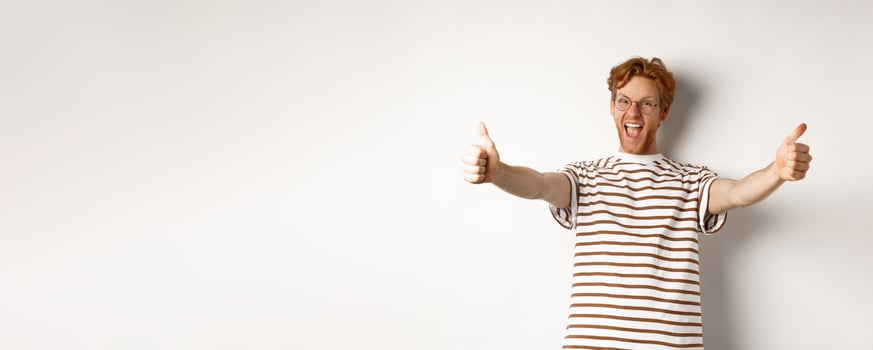 Happy redhead man scream yes and showing thumbs-up, approve and praise excellent company, standing over white background photo
