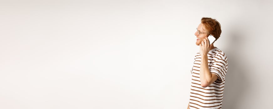 Profile of happy young handsome man talking on mobile phone, looking left and smiling, standing over white background photo