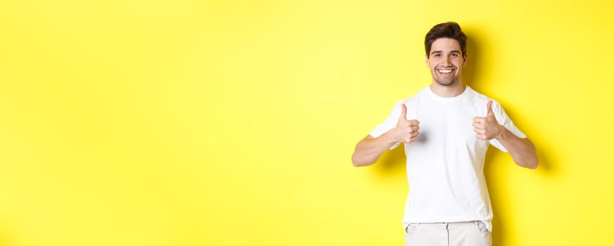 Portrait of happy man showing thumbs-up in approval, like something or agree, standing over yellow background photo