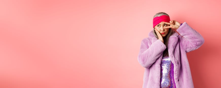 Fashion and shopping. Stylish and funky asian female model, showing peace signs and looking cute and silly, posing in purple faux fur coat over pink background photo